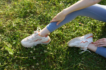 Young woman in comfortable sportswear stretching in grass wearing trendy sneakers, evoking a sense...