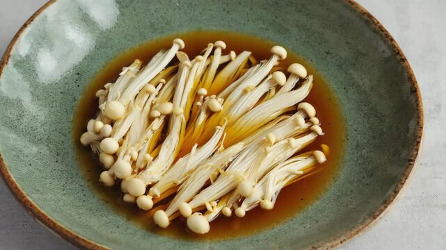 Steamed enoki mushrooms in soy-based broth served in ceramic bowl