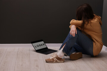 Cyber bullying. Upset teenage girl and laptop with text You Loser on floor indoors. Space for text