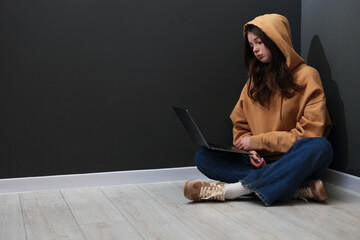 Cyber bullying. Upset teenage girl with laptop on floor indoors. Space for text