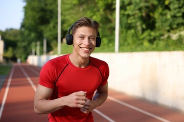 Sporty man with headphones running at stadium, space for text