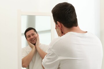 Handsome man looking at himself in mirror indoors