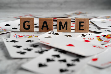 The word "GAME" spelled out with wooden letter blocks amidst a scatter of playing cards, illustrating leisure and entertainment