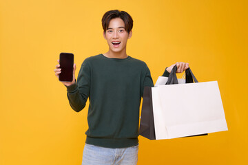 excited Asian man proudly displays a smartphone with a blank screen while holding shopping bags...