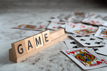 Wooden letter blocks spelling "GAME" on a wooden rack, with playing cards scattered around on a textured surface