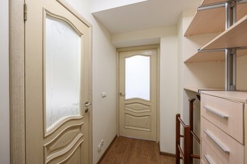 well-lit hallway with two ornate wooden doors featuring frosted glass panels. A closet organizer...