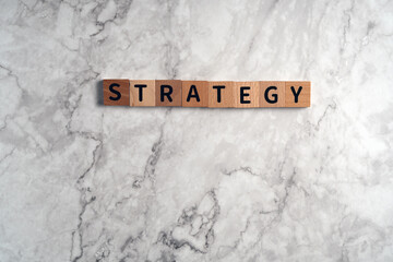 The word "STRATEGY" spelled out with individual wooden letter blocks arranged on a classic white marble textured background