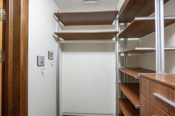 walk-in closet features wood shelves with metal frames, a wooden door with brass hinges, and small...