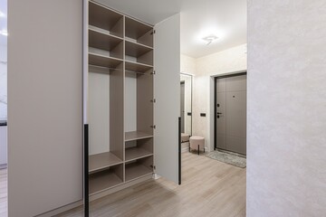 view of an apartment entrance. An open closet is on the left, revealing shelving and hanging rods. A front door, mirror, and pouf are on the right side of the image