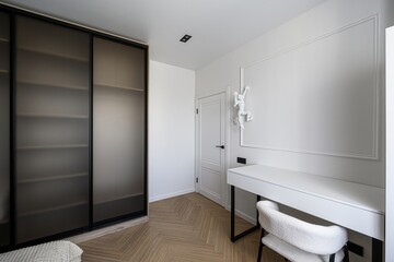 Minimalist room featuring a wardrobe with frosted glass doors, white desk, fluffy chair,...