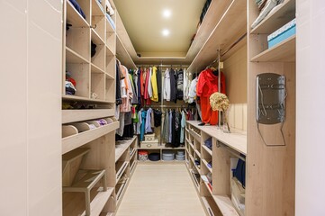 well-organized walk-in closet with wooden shelves and hanging rods filled with clothes and...