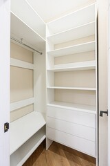 bright, open walk-in closet featuring white shelves, drawers, and a hanging rod. Wood flooring adds...