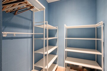 empty walk-in closet with blue walls and white shelves. Some wooden hangers can be seen above the...