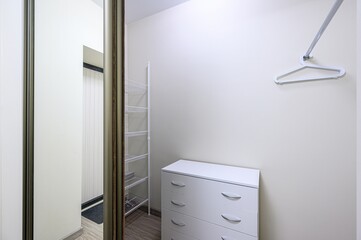well-organized closet with white drawers, shelving, and a hanger. Mirror door reflects a glimpse of...
