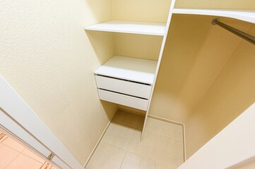 closet interior with shelves, two white drawers, and a hanging rod. The walls are light beige, and...