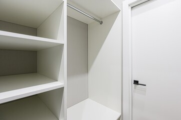 interior shot featuring a clean, white, and minimalist closet with shelves, a hanging rod, and a...