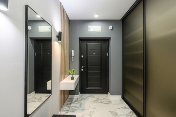 modern entryway featuring a black door, mirror, wood slat wall, marble floor, and sliding closet