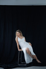 Beautiful pregnant young blonde in a long white silk dress to the floor on a black fabric...