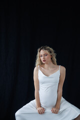Beautiful pregnant young blonde in a long white silk dress to the floor on a black fabric...