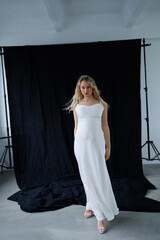 Beautiful pregnant young blonde in a long white silk dress to the floor on a black fabric...