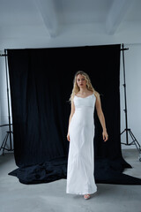 Beautiful pregnant young blonde in a long white silk dress to the floor on a black fabric...