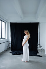 Beautiful pregnant young blonde in a long white silk dress to the floor on a black fabric...