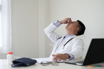 An asian young doctor is getting headache after duty and hand holding and rubbing hurt area,...