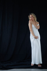 Beautiful pregnant young blonde in a long white silk dress to the floor on a black fabric...