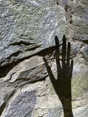 Shadow of human hand on rough stone wall in daylight with strong contrast and textured surface