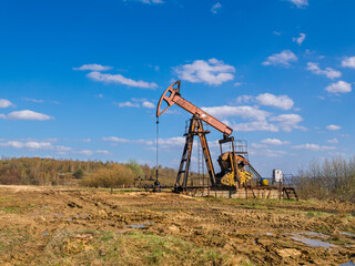 Traditional oil derrick on muddy terrain with dramatic sky and distant woodland scenery