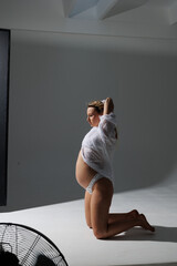 Beautiful pregnant young blonde in white shirt on cyclorama with beautiful lighting. Pregnant girl...