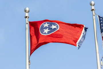 The Tennessee state flag on a flag pole blowing in the wind with a blue sky background.