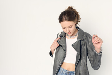 a woman dressed in accordance with fashion trends, in a leather jacket and a white top poses...
