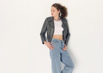 a woman dressed in accordance with fashion trends, in a leather jacket and a white top poses...
