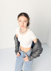 a woman dressed in accordance with fashion trends, in a leather jacket and a white top poses...
