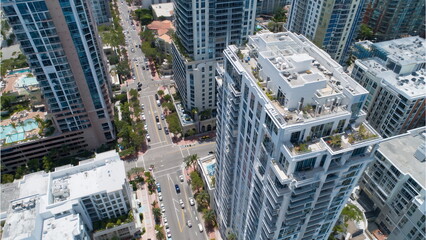 Daytime drone shot aerial view of a high-rise condominium building in an urban area, showing balconies, streets filled with cars, green trees and landscaping.
