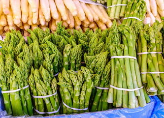 Fresh asparagus and other vegetables displayed at a market stall during morning hours in the spring...
