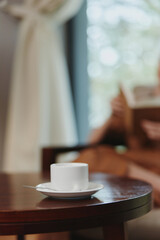 Relaxing moment with a cup of coffee on a wooden table by a window, showcasing tranquility, indoor lifestyle, and a warm atmosphere with soft natural light