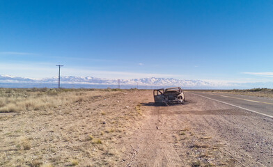 Burnt remains of a pickup truck by an asphalt road in the desert.