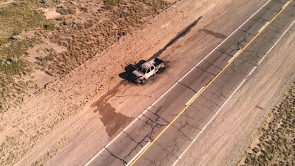Burnt remains of a pickup truck by an asphalt road in the desert. Aerial view. No AI.