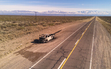 Burnt remains of a pickup truck by an asphalt road in the desert. Aerial view. No AI.