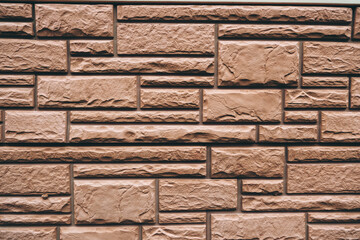 Textured brown stone brick wall with geometric arrangement and rugged surface. Architectural pattern background for construction, renovation, building, and interior design themes.