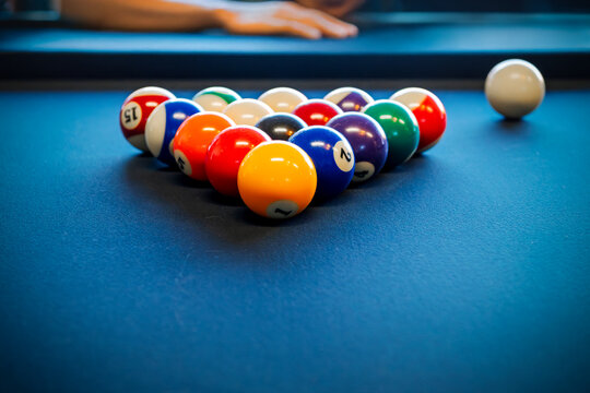 Billiard balls are racked in the starting setup for a game on a blue slate top pool table.