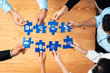 A group of diverse individuals collaboratively assembles blue puzzle pieces, each featuring symbols...
