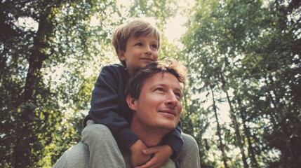 Father giving son ride on back in park. Portrait of happy father giving son piggyback ride on his shoulders and looking up. Cute boy with dad playing outdoor., no logos, no brands