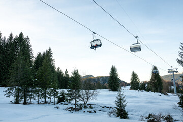 A ski lift with two cars on it is suspended above a snowy field