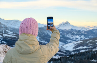 A woman wearing a pink hat is taking a picture of a mountain range