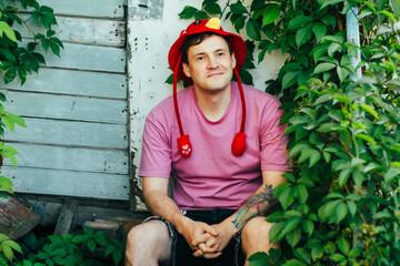 A young man wearing a bright red hat sits comfortably amid lush green leaves He appears relaxed and...