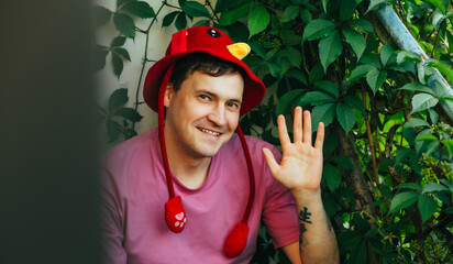 A cheerful man with a friendly demeanor waves his hand while sitting in a garden full of green...