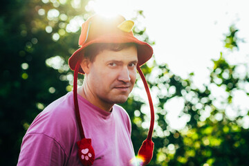 Man Wearing a Red and Yellow Playful Hat Enjoys Sunny Outdoor Moment Surrounded by Trees in a Park